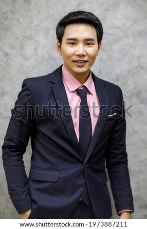 Handsome businessman wearing pink shirt, tie, suit in black, standing smiling, looking camera, right hand in pant pocket. Photo id shooting in studio with a loft background