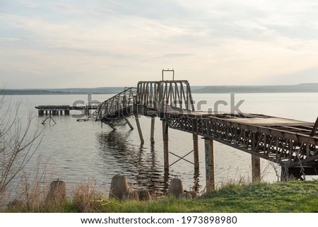 Abandoned iron pier or jetty on the river bank. The pier is already badly destroyed and is sinking in water.
