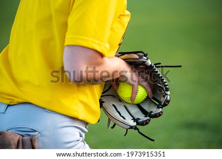 Close-up of a softball player's hand grasping a ball inside a baseball glove.