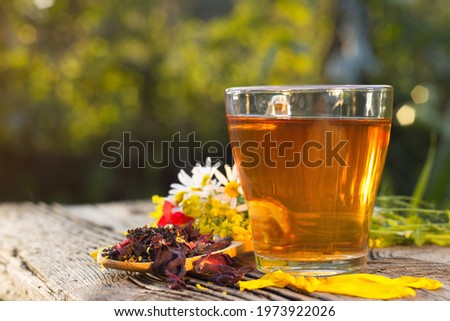Still life with herbal tea ( black and hibiscus tea, calendula, cloves, cardomon, cinnamon ) on a blurred background.
Prepared and dry tea, rose petals and chamomile are on an old wooden table.