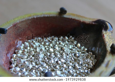 A ceramic crucible or melting pot with grains of sterling silver 925 for jewelry making after hand smelting in a workshop. One of the two major precious metals on the market. Royalty-Free Stock Photo #1973929838