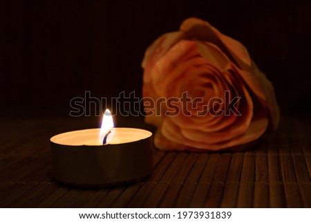 burning candle and rose against dark background for copy space. tea light and rose, close up concept for love, memorial, hope