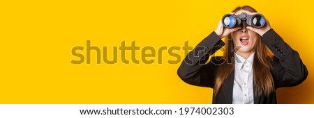 surprised young business woman looking through binoculars on yellow background. Royalty-Free Stock Photo #1974002303