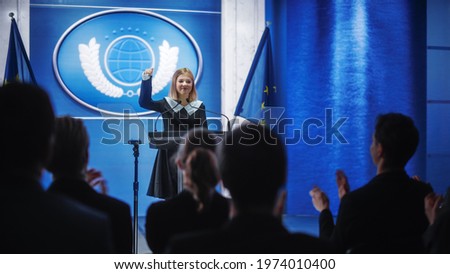 Young Girl Activist Delivering an Emotional and Powerful Speech at Press Conference in Government Building. Child Speaking to Congress at Summit Meeting. Backdrop with European Union Flags. Royalty-Free Stock Photo #1974010400