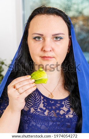 A Jewish woman with her head covered in a blue cape at the Passover Seder table is eating moror hazeret matzah. Vertical photo