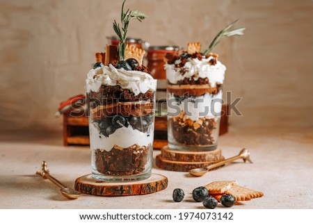 Two glasses with a layered dessert trifle with chocolate, cream, cookies and blueberries Royalty-Free Stock Photo #1974073142