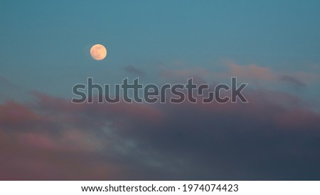 Pink clouds after sunset with bright moon shines in the background.