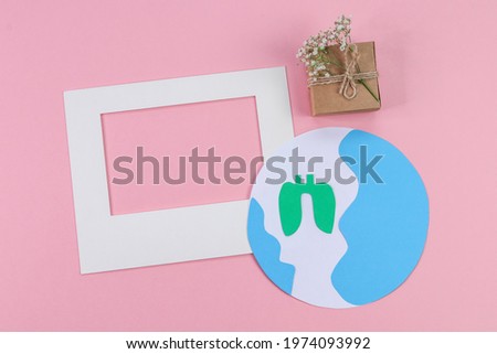 
Empty frame, gift with flowers and creative paper planet on pink background with space for text, top view close-up.