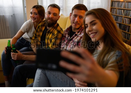 A group of friends hanging out together at a house party and drinking beer while taking a selfie with a smartphone and having fun
