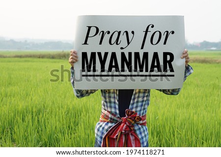 Text " Pray for Myanmar" on paper board hold by a man at green paddy field. Concept protesting for democracy and against the coup in Myanmar. Royalty-Free Stock Photo #1974118271