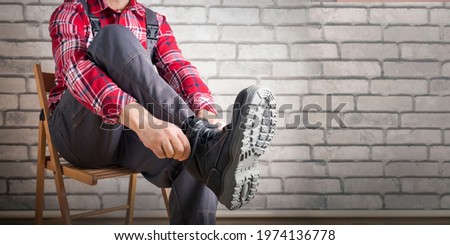 Buider putting on shoes for work near brick wall. Safety work concept. Banner. Royalty-Free Stock Photo #1974136778