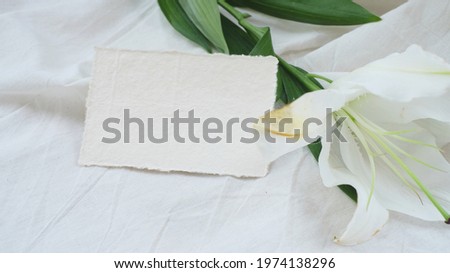 Photostock wedding styled composition. Feminine desktop mockup scene with leaves, lily flower, silk ribbon, blank greeting card on white textured fabric background.