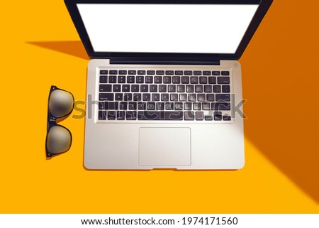 Top view of modern laptop isolated on yellow background with modern sunglasses.