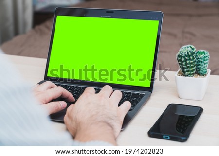 Young businessman working on laptop in home, rear view green screen of business man hands busy using laptop at office desk, typing on computer sitting at wooden table