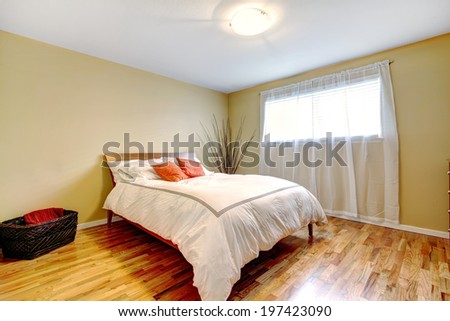 Ivory tones bedroom with light window, modern bed in white and orange colors. Room decorated with dry branches and wicker basket