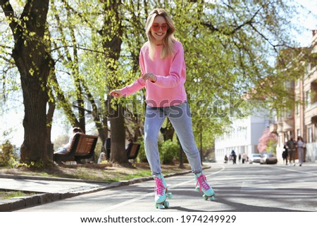 Beautiful young woman roller skating outdoors on sunny day