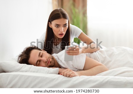 Jealousy Problem. Shocked Girlfriend Reading Messages On Cheating Husband's Phone Suspecting Infidelity In Bedroom At Home. Jealous Girlfriend Checking Boyfriend's Smartphone. Selective Focus Royalty-Free Stock Photo #1974280730
