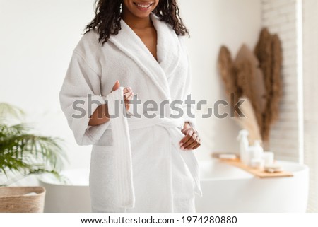 Unrecognizable African American Lady Untying White Bathrobe Preparing For Beauty Ritual Standing In Modern Bathroom In Hotel Spa Center. Female Beauty And Body Care. Cropped Royalty-Free Stock Photo #1974280880