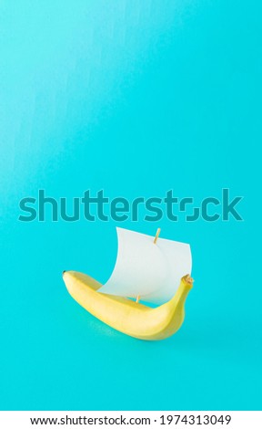 Advertisement idea with a yellow banana like a ship and a sail of paper against pastel blue background. Minimal summer nature concept in vertical orientation.