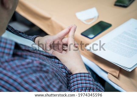 Man in a business suit sitting at a desk with his hands together, with some documents and a smartphone in front of him