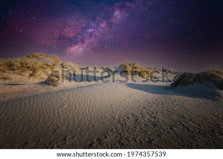 Night image of dune landscape with starry sky with purple and violet starlight against dark blue sky background