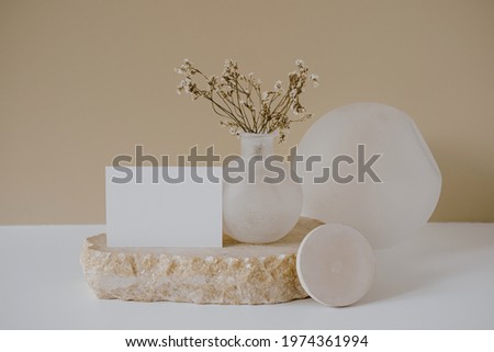 Blank paper sheet card with mockup copy space, dry flowers, marble stone against neutral beige wall. Minimal aesthetic business brand, blog, social media template background