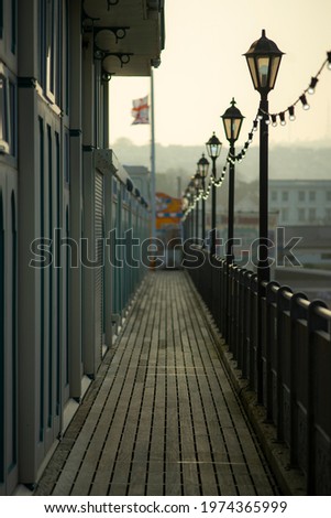 Vertical image of the boardwalk of a pier. Photo taking while standing on the pier. Floor is wooden textured. Lined with old vintage street lights. It's evening at a seaside coastal town. Background.