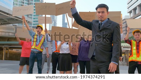 Asian - Thai young handsome man screaming in megaphone at protest for human rights outdoors in smoke. Group of people protesting at street. Strike against violence. Hands clenched into a fist.
