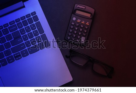 Laptop, glasses, calculator in neon light. Top view.