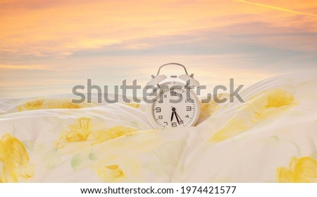 Clock on the bed. Alarm clock on the duvet, pillow with sunrise - dawn sky background in the morning. Advertising concept, copy space.