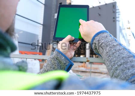 A man holds a tablet with a green screen in his hands against the backdrop of a building under construction. Architect or designer