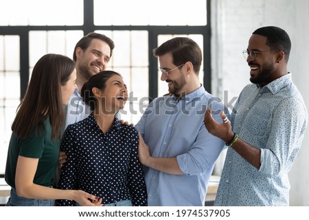 Happy coworkers congratulating excited Indian female employee with hiring or job promotion, welcoming intern to team hugging and cheering. Staff expressing respect and recognition to promoted coworker Royalty-Free Stock Photo #1974537905