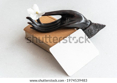 close-up of Buddha's hand holding a white flower on a old book and with empty paper for your text on marble table. Royalty-Free Stock Photo #1974539483