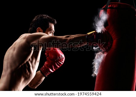 Strong muscular man punching a bag with boxing gloves on a black background Royalty-Free Stock Photo #1974559424