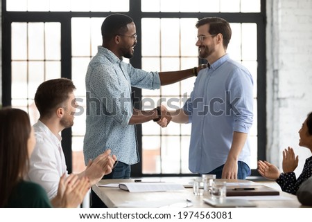 Happy African American male boss welcoming new hired employee, team applauding. Business leader expressing recognition, appreciation, acknowledge, giving handshake to proud worker Royalty-Free Stock Photo #1974563081