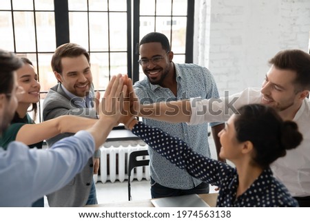 Excited millennial teammates joining hands for giving high fives. Team of happy employees celebrating corporate goal achievement, successful project accomplishment, shared success. Teamwork concept Royalty-Free Stock Photo #1974563138