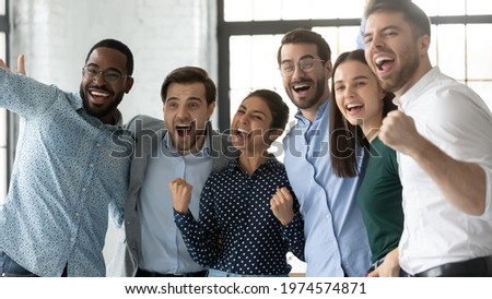 Multiethnic team of excited employees celebrating corporate achievement, high sales result, work success, shouting for joy. Happy diverse professionals hugging, laughing, making winner gestures Royalty-Free Stock Photo #1974574871