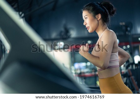 Asian young athlete sportswoman practice workout to maintain muscle in gym or fitness club. Active attractive girl in sport wear exercise by run on Treadmill to burns calories for health in stadium Royalty-Free Stock Photo #1974616769