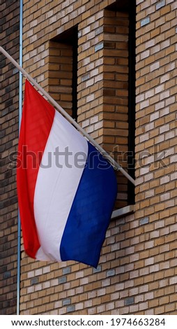 Closeup of Dutch national flag hanging half mast on the exterior facade of a modern building in commemoration of those fallen in war times