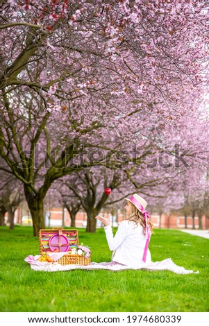 Beautiful woman in straw hat under blooming cherry trees in picnic place. Girl wearing a pink long skirt in spring garden