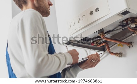 Professional plumber servicing a boiler and writing on a clipboard Royalty-Free Stock Photo #1974683861