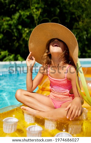 Portrait of little girl in hat relaxing in swimming pool, swims on inflatable yellow mattress and has fun in water on family vacation, tropical holiday resort.