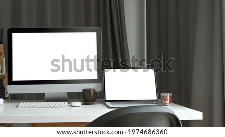 Home office desk with mock up computer and laptop with blank white screen.