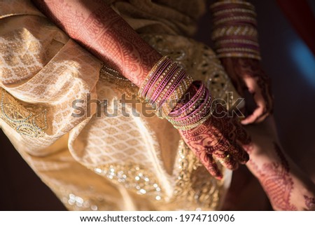 The hands with bracelets and henna tattoos correcting the hem of the dress