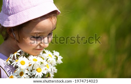 Little girl with a bouquet of daisies in summer on a natural background. Happy child,panama hat for sun protection. International Children's Day. Copy space. Authenticity, rural life, eco-friendly