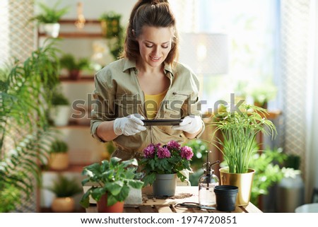Green home. happy modern woman in white rubber gloves with potted plant making photos using smartphone at modern home in sunny day.