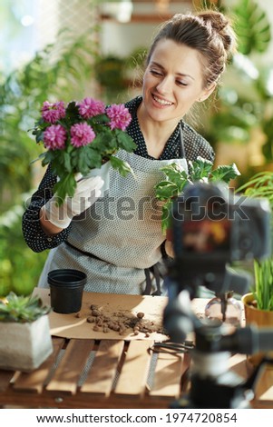 Relaxing home gardening. happy modern woman in white rubber gloves with potted plant records gardening educational video tutorials in the modern living room in sunny day.