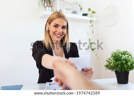 Two business people shaking hands over a desk as they close a deal or partnership, focus to a smiling young blond woman