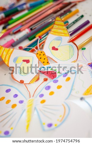 Top view of colorful, kid-drawn pictures, felt-tip pens and pencils on a white table. Creative ideas, creativity and early learning. Education concept. Selective focus