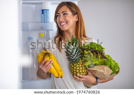Closeup of a cheerful young couple picking some fruit and veggies from the fridge to make some healthy breakfast on Sunday morning. A side-view shot of a mature caucasian woman taking something 